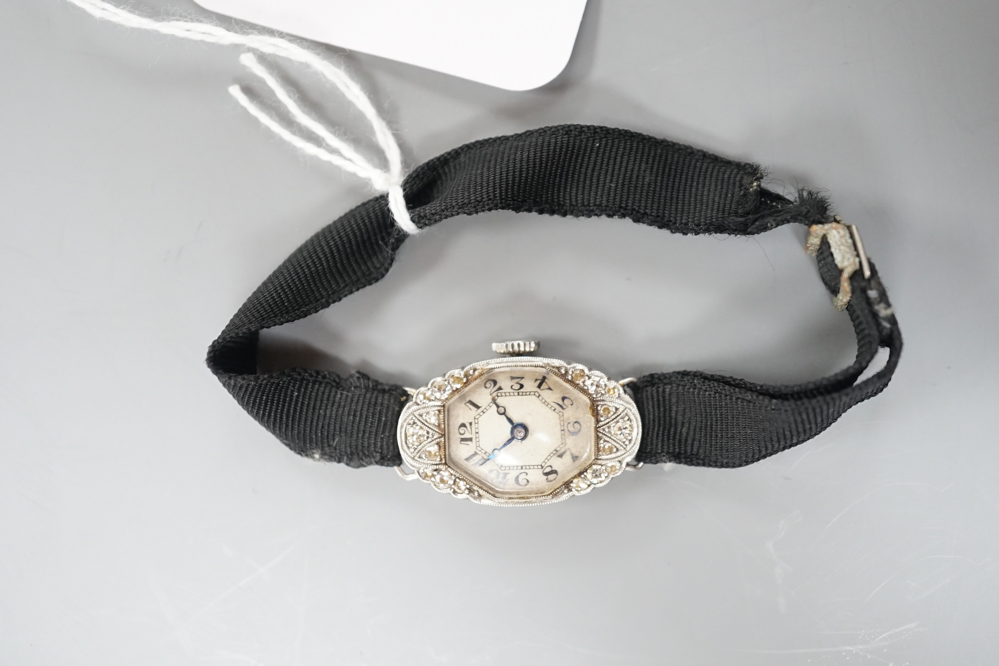 A lady's white metal (stamped platine) and diamond set oval cocktail watch, on a black sash bracelet, gross weight 13.9 grams.